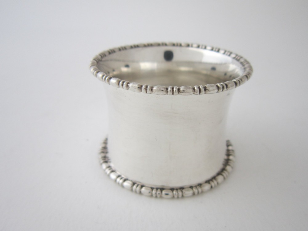 A cylindrical George V sterling silver napkin ring featuring decorative beaded rims along both edges and stamped British hallmarks on the outer surface. View II