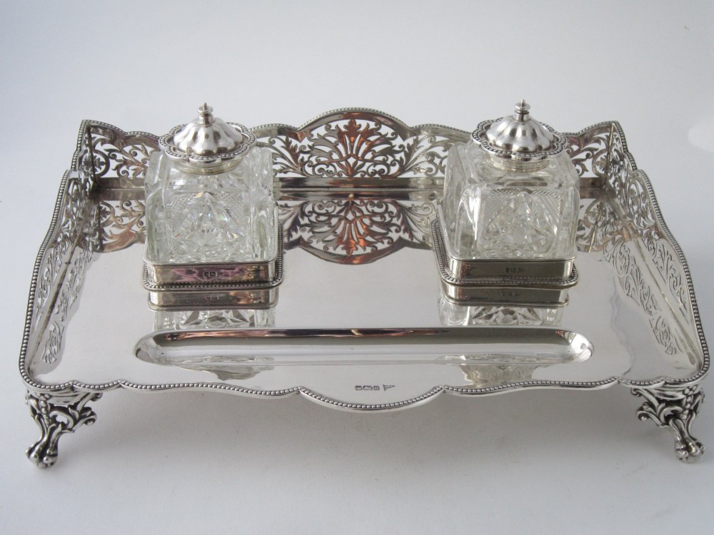 A George V sterling silver tray featuring a pierced gallery, scroll feet, a central pen recess, and two square cut-glass inkwells with silver lids. View II