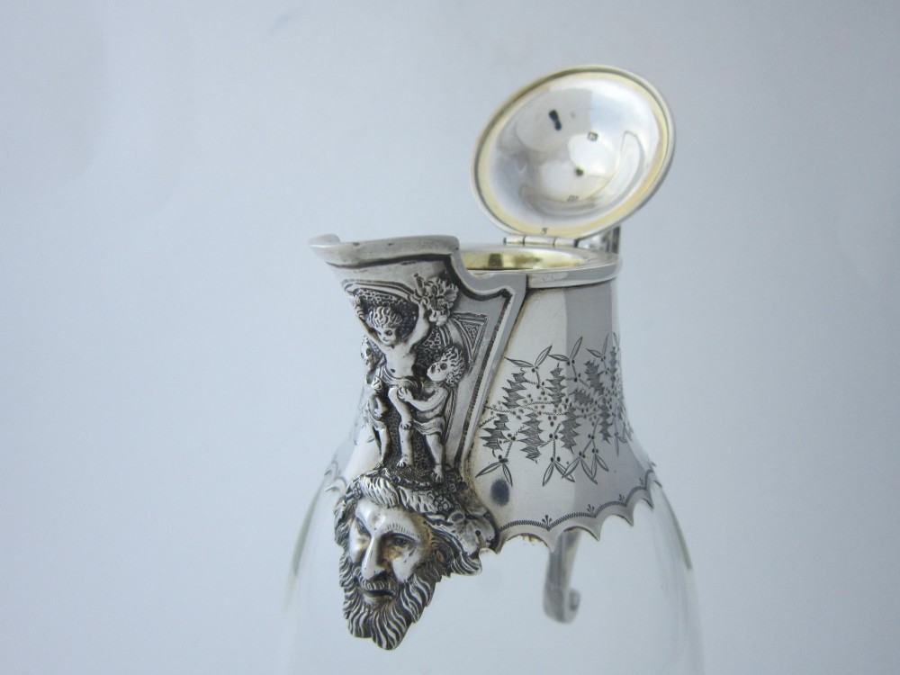 A Victorian clear glass claret jug with an engraved sterling silver collar, hinged lid with finial, and an ornate scroll handle. View III