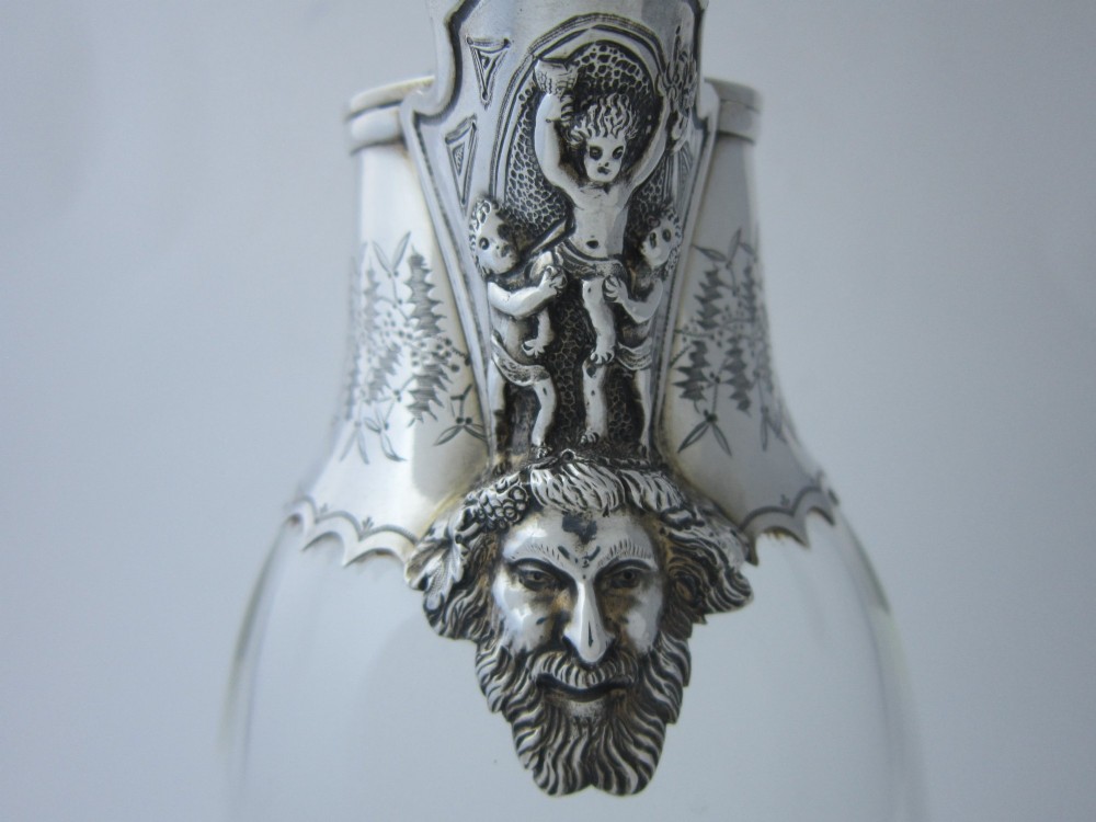 A Victorian clear glass claret jug with an engraved sterling silver collar, hinged lid with finial, and an ornate scroll handle. View IV