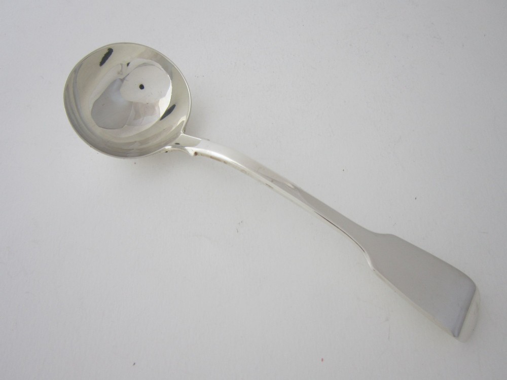 A Victorian sterling silver sauce ladle featuring a fiddle pattern handle and a round deep bowl, displayed on a plain white surface.