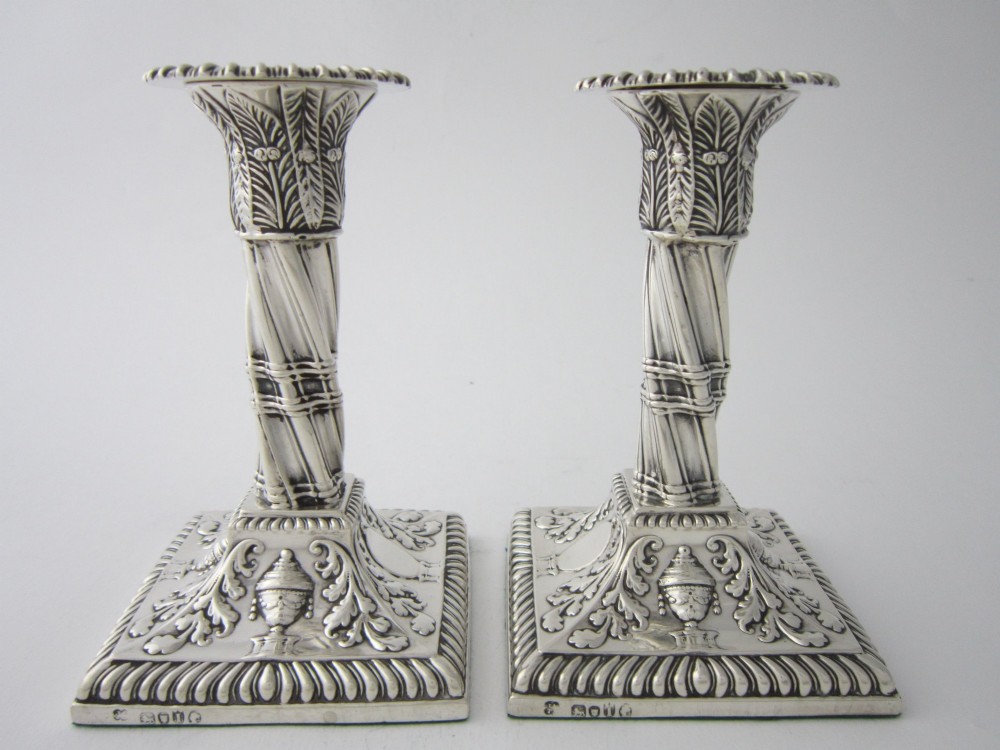 Pair of 1884 Victorian sterling silver candlesticks featuring spiral fluted column stems and square bases embossed with urn and leaf motifs.