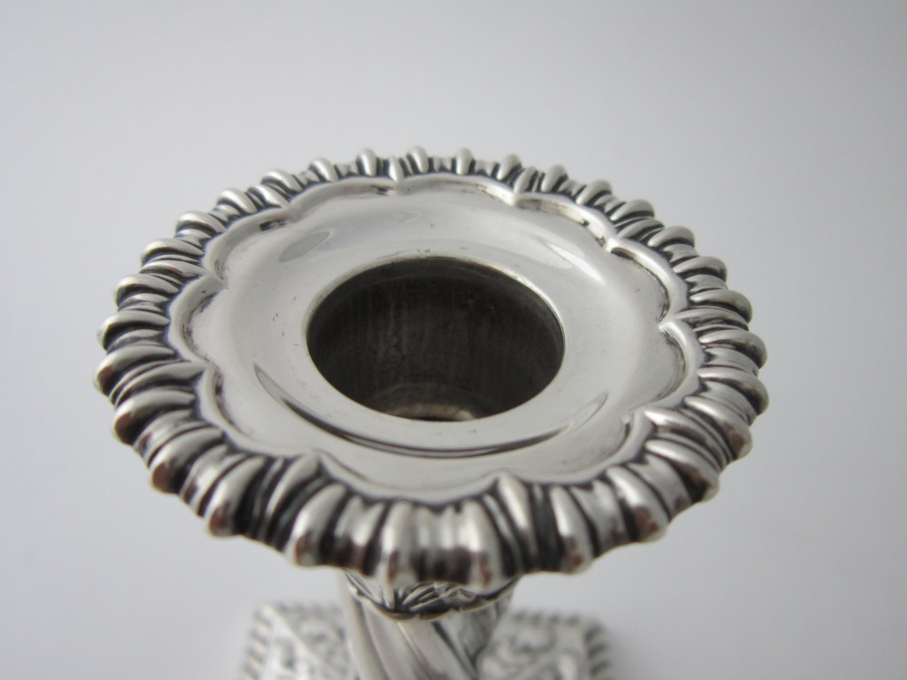 Pair of 1884 Victorian sterling silver candlesticks featuring spiral fluted column stems and square bases embossed with urn and leaf motifs. View IV