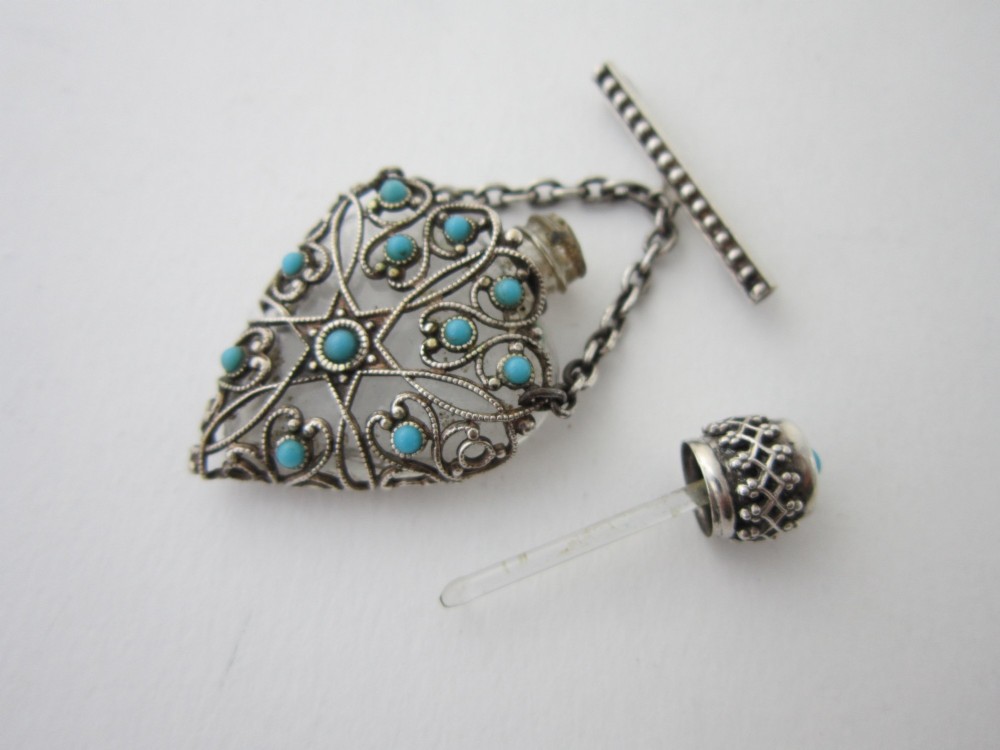 A 1920s Continental silver scent bottle featuring clear glass enclosed in silver filigree overlay set with turquoise cabochons, suspended from a beaded bar pin. View IV