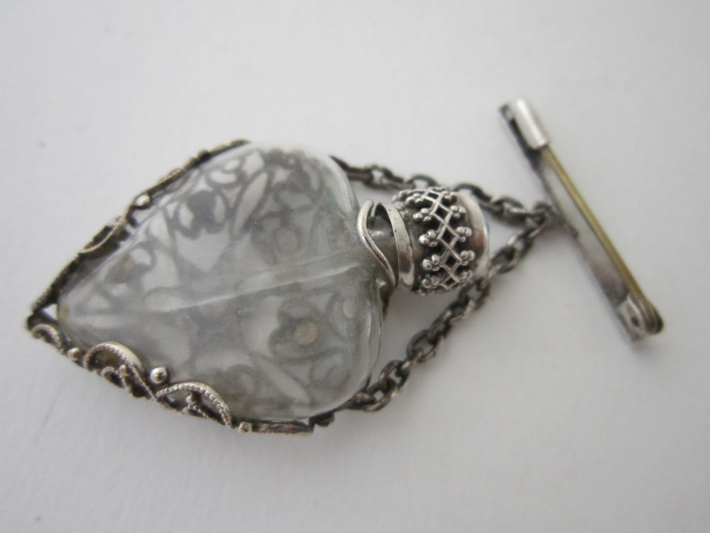 A 1920s Continental silver scent bottle featuring clear glass enclosed in silver filigree overlay set with turquoise cabochons, suspended from a beaded bar pin. View V