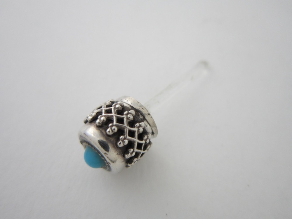 A 1920s Continental silver scent bottle featuring clear glass enclosed in silver filigree overlay set with turquoise cabochons, suspended from a beaded bar pin. View VII