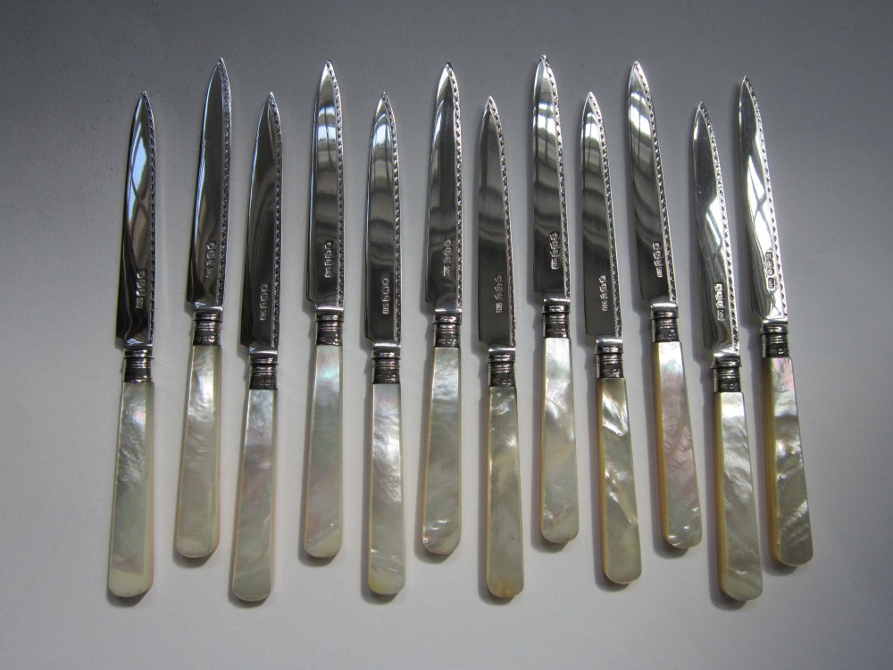 An open fitted wooden canteen displaying a set of sterling silver dessert knives and forks with mother-of-pearl handles set against a green velvet lining. View II