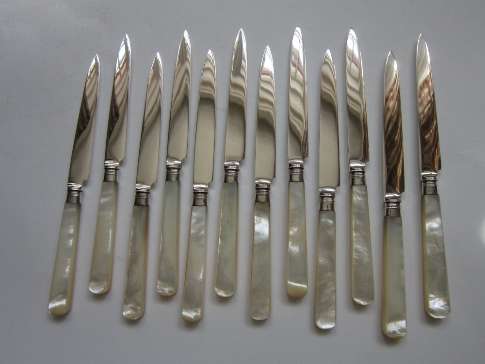 An open fitted wooden canteen displaying a set of sterling silver dessert knives and forks with mother-of-pearl handles set against a green velvet lining. View III