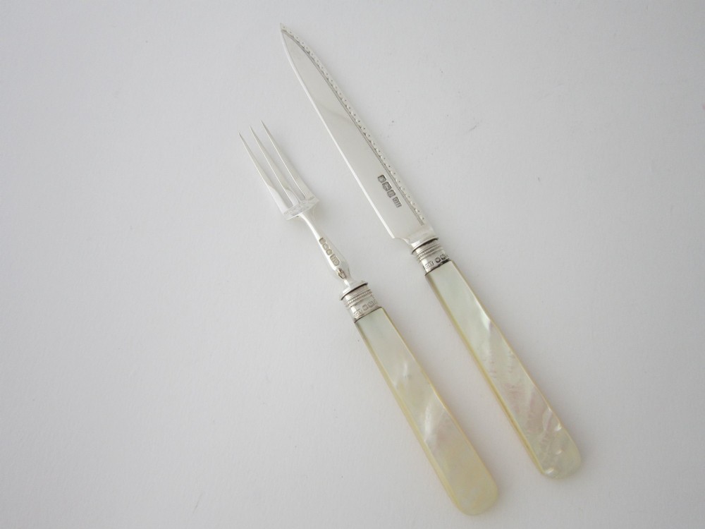 An open fitted wooden canteen displaying a set of sterling silver dessert knives and forks with mother-of-pearl handles set against a green velvet lining. View VI