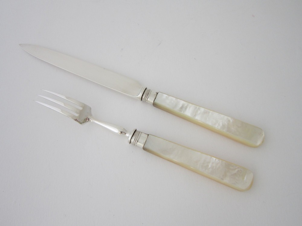 An open fitted wooden canteen displaying a set of sterling silver dessert knives and forks with mother-of-pearl handles set against a green velvet lining. View VII