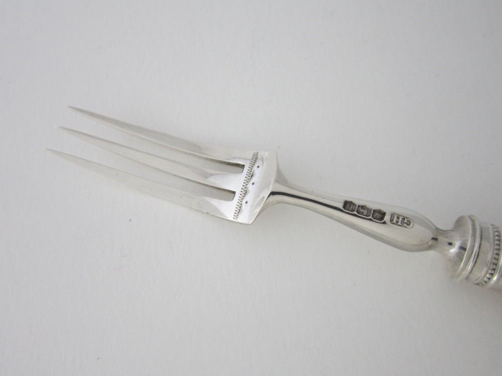 An open fitted wooden canteen displaying a set of sterling silver dessert knives and forks with mother-of-pearl handles set against a green velvet lining. View X