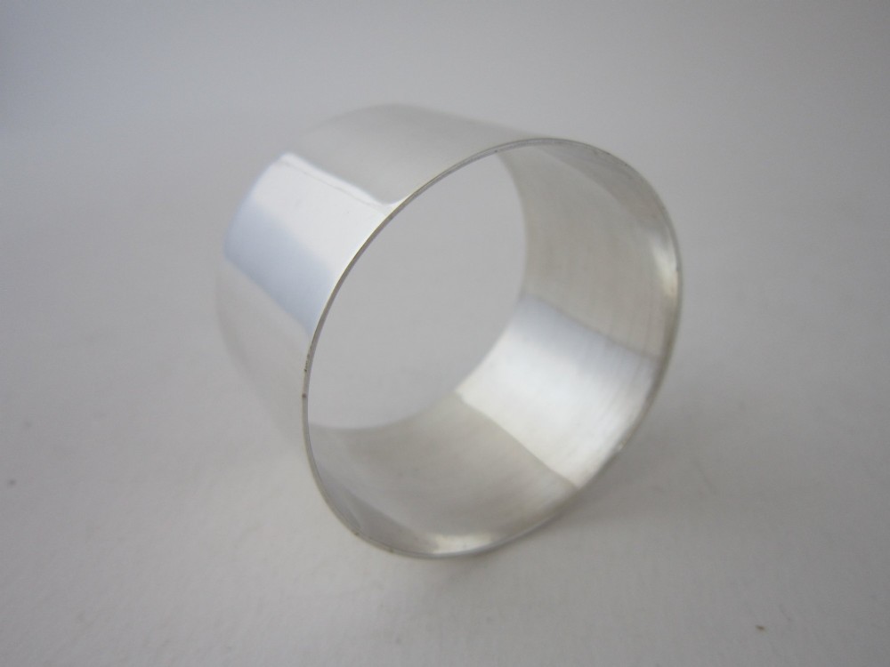 A plain, highly polished circular sterling silver napkin ring resting upright on a white surface.
