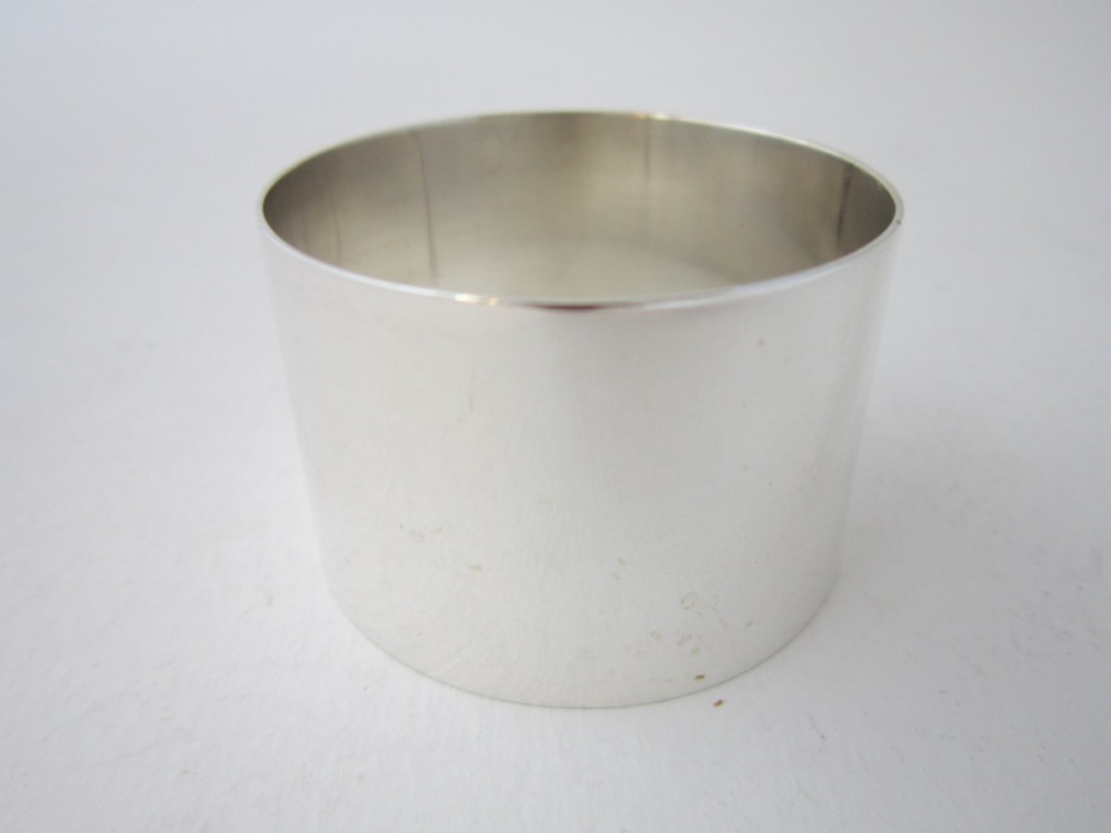 A plain, highly polished circular sterling silver napkin ring resting upright on a white surface. View II