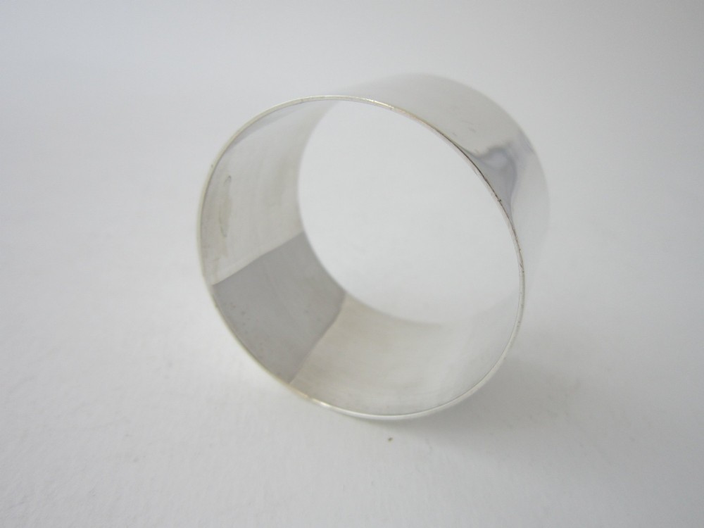 A plain, highly polished circular sterling silver napkin ring resting upright on a white surface. View III