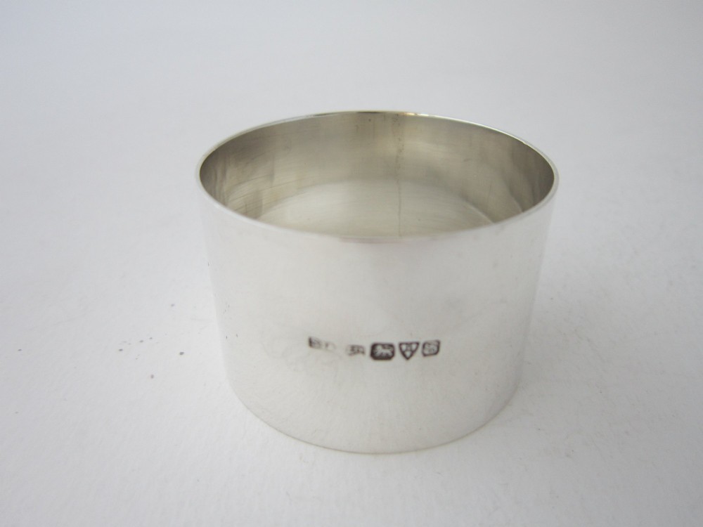 A plain, highly polished circular sterling silver napkin ring resting upright on a white surface. View IV