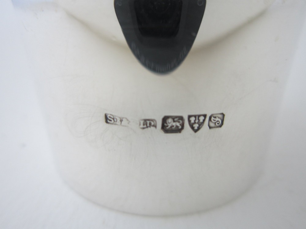 A plain, highly polished circular sterling silver napkin ring resting upright on a white surface. View V