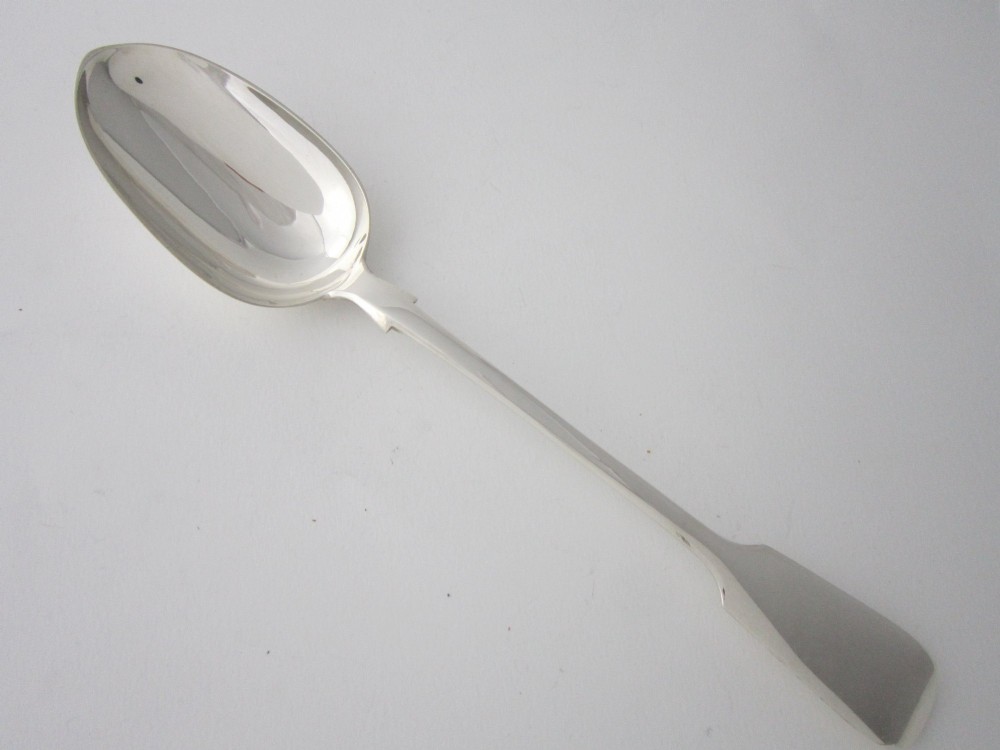 An antique Victorian sterling silver basting spoon featuring a fiddle pattern handle and polished oval bowl.