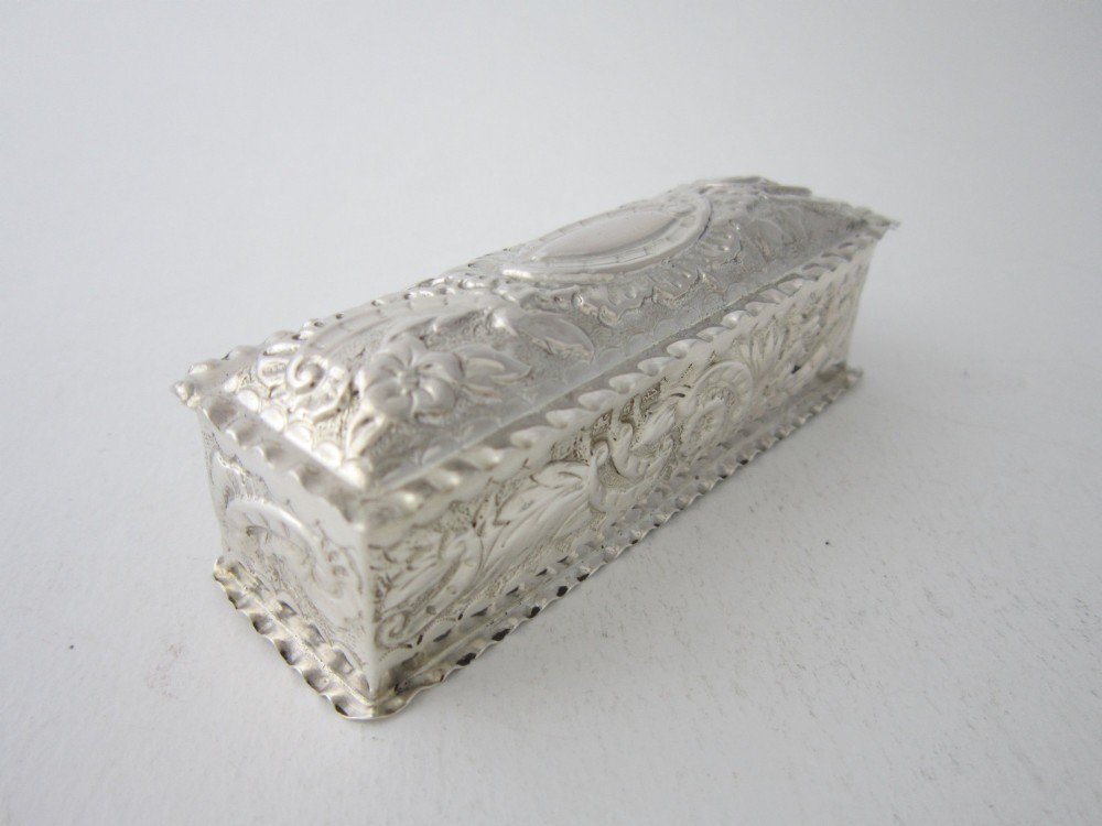 A small rectangular Victorian sterling silver trinket box featuring embossed floral scrolls, scalloped edges, and a blank central cartouche on the hinged lid. View II