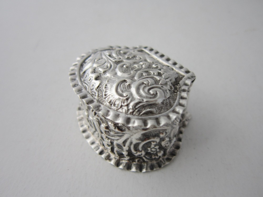 An oval Victorian sterling silver pill box decorated with embossed scrollwork and crimped fluted rims on the lid and base. View II