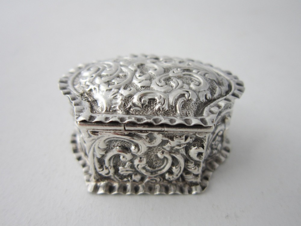 An oval Victorian sterling silver pill box decorated with embossed scrollwork and crimped fluted rims on the lid and base. View III