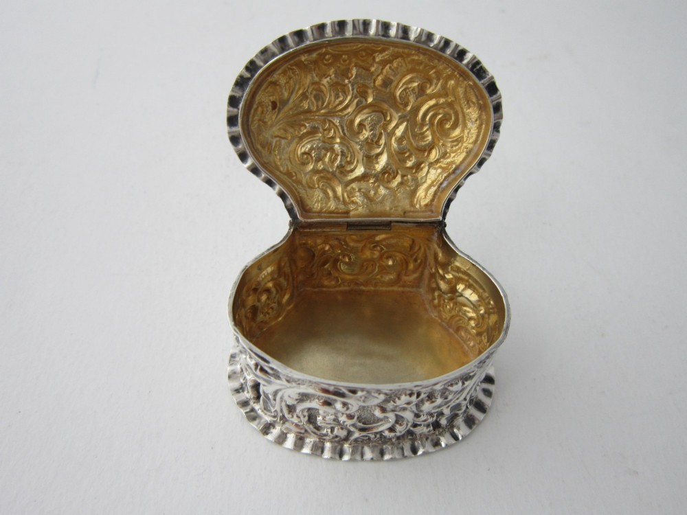 An oval Victorian sterling silver pill box decorated with embossed scrollwork and crimped fluted rims on the lid and base. View V