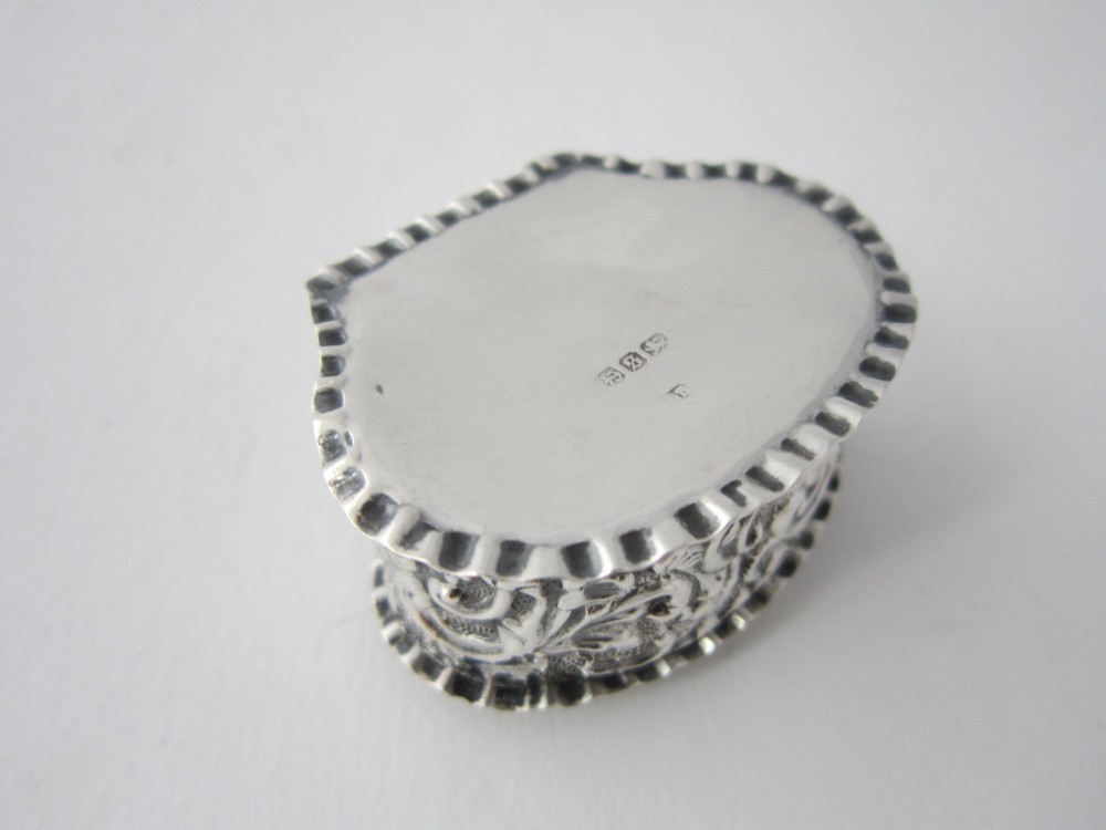 An oval Victorian sterling silver pill box decorated with embossed scrollwork and crimped fluted rims on the lid and base. View VI