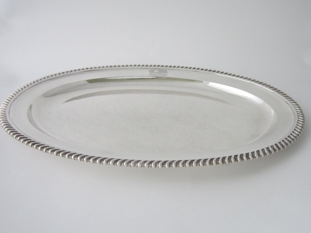 An oval William IV sterling silver meat platter featuring a decorative gadrooned border and an engraved coat of arms on the upper rim. View II