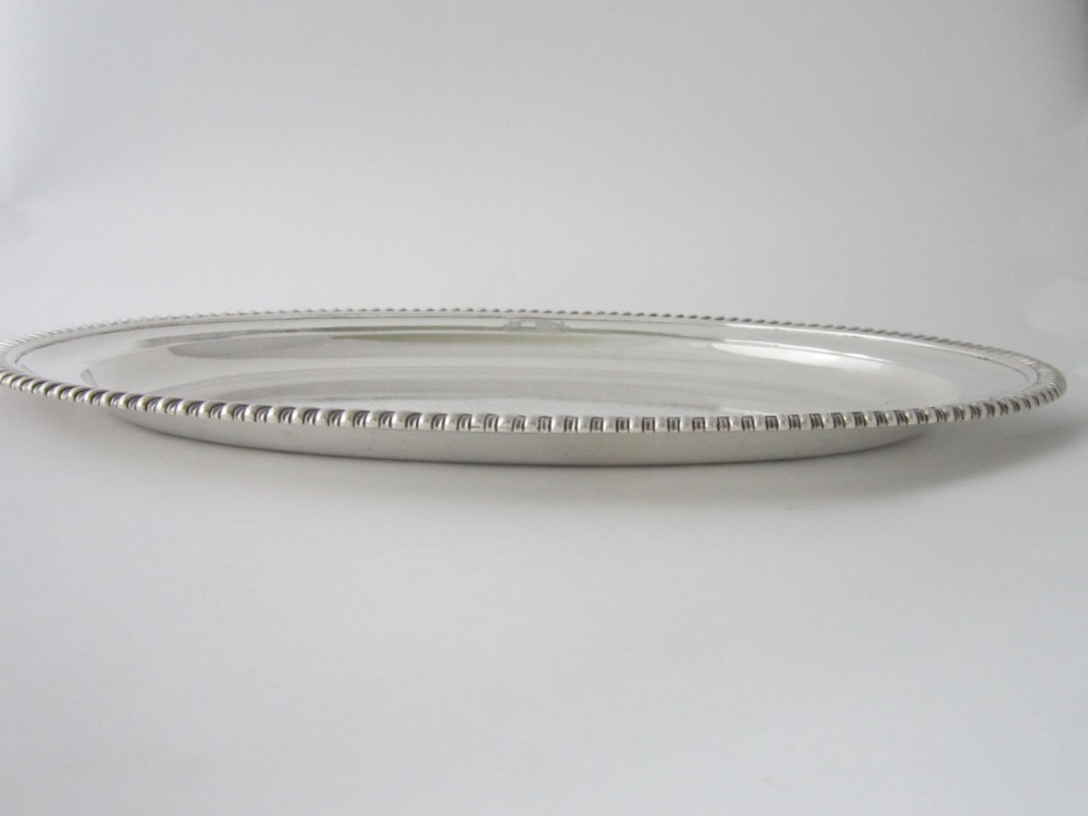 An oval William IV sterling silver meat platter featuring a decorative gadrooned border and an engraved coat of arms on the upper rim. View III