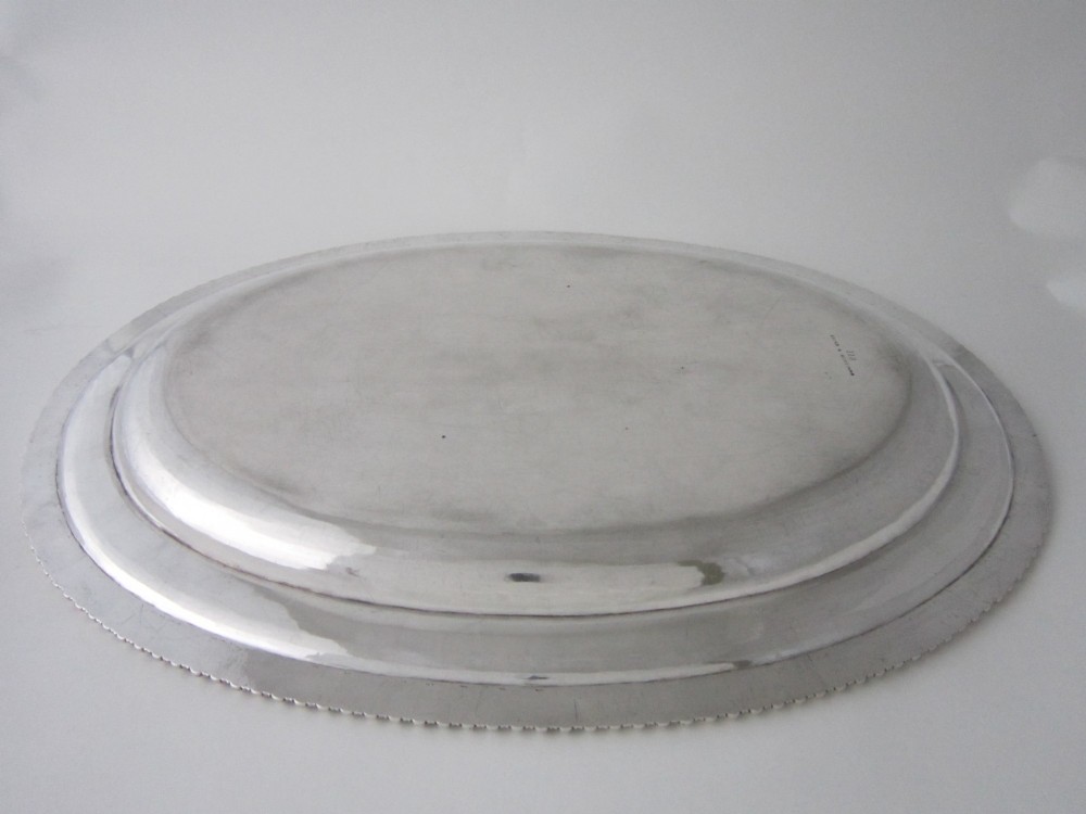 An oval William IV sterling silver meat platter featuring a decorative gadrooned border and an engraved coat of arms on the upper rim. View V