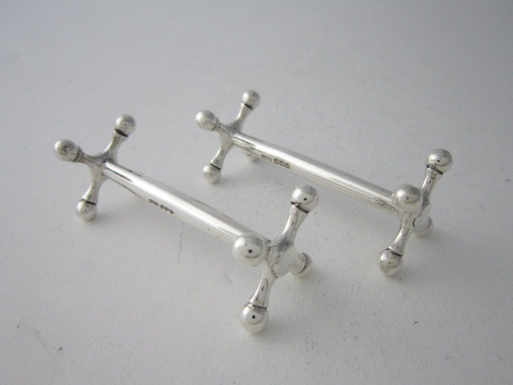A pair of hallmarked sterling silver knife rests with crossed spherical end supports connected by a smooth central bar.