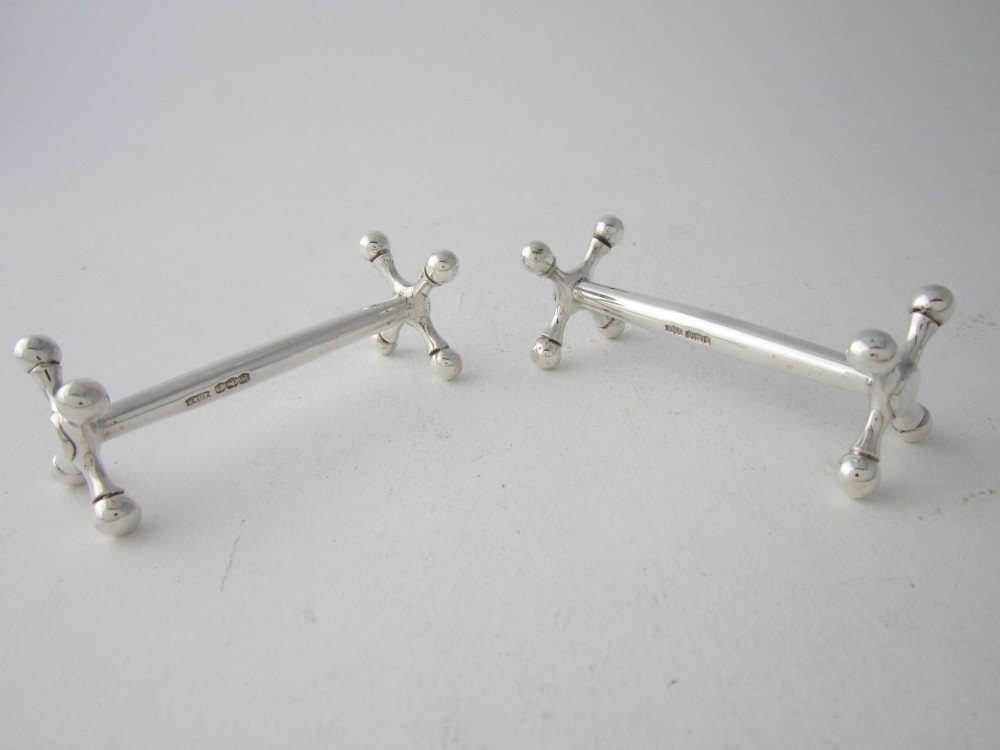 A pair of hallmarked sterling silver knife rests with crossed spherical end supports connected by a smooth central bar. View II