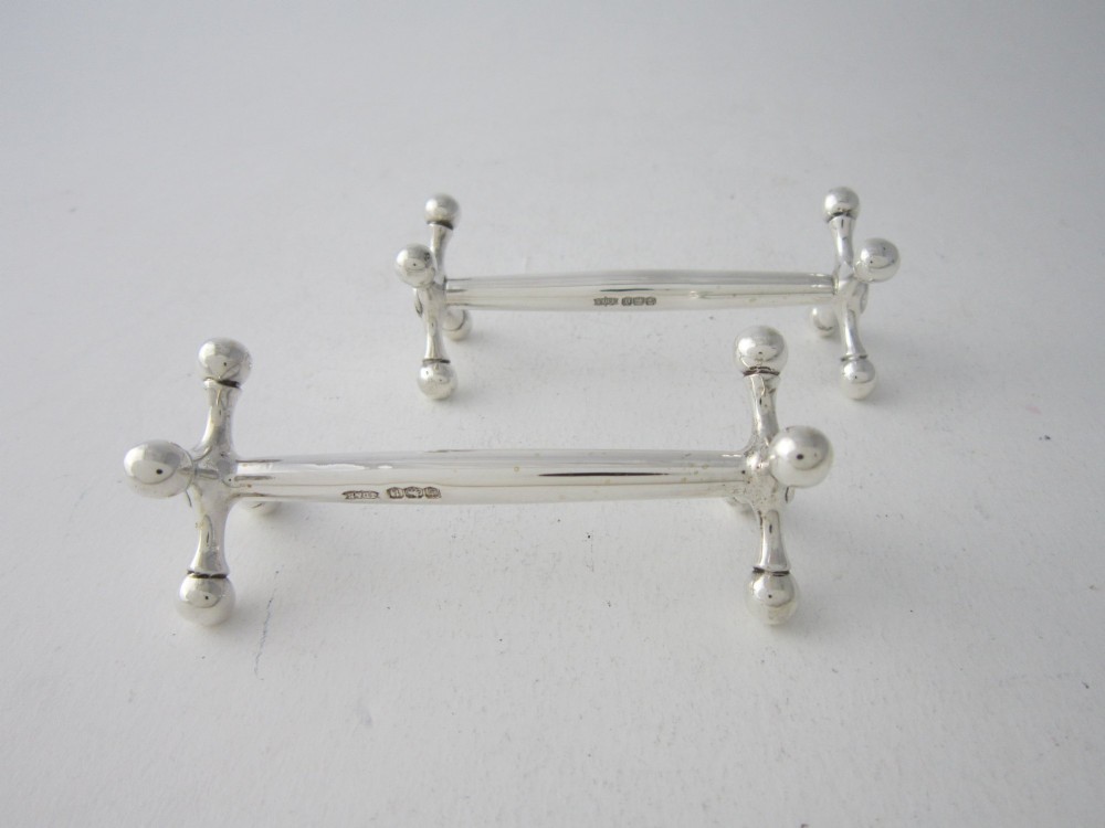 A pair of hallmarked sterling silver knife rests with crossed spherical end supports connected by a smooth central bar. View III