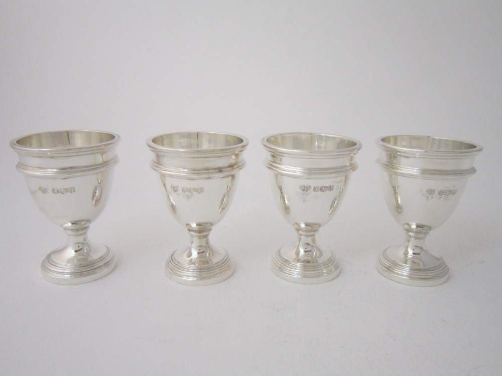An antique George V sterling silver egg cruet featuring a central carrying handle, six egg cups, and matching spoons arranged on an oval tray base. View VIII