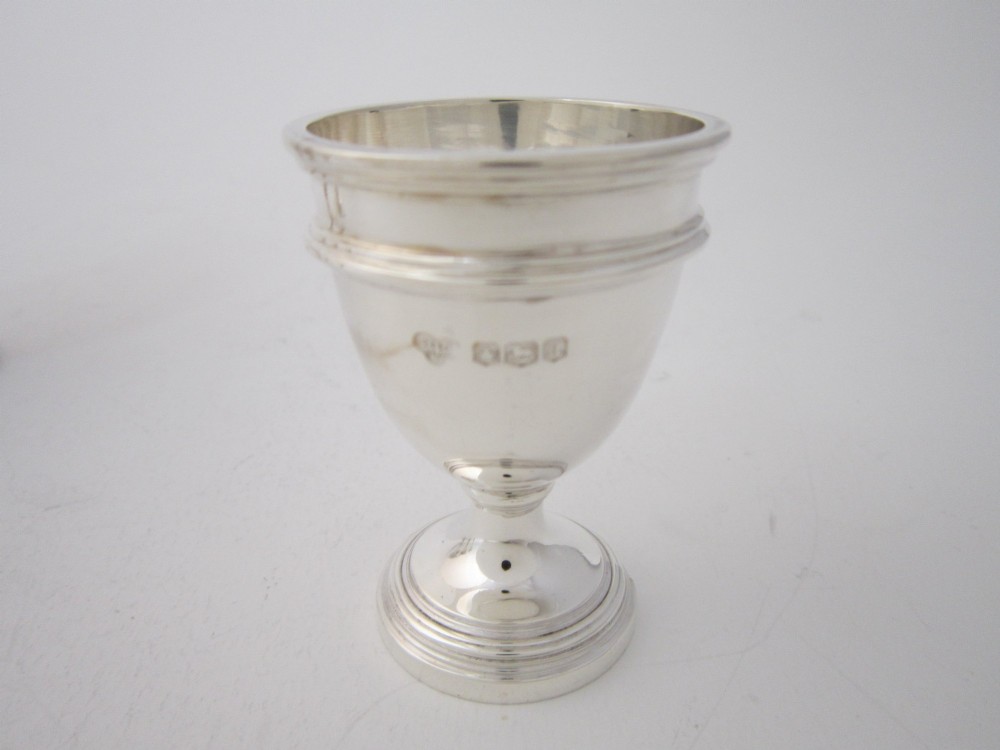 An antique George V sterling silver egg cruet featuring a central carrying handle, six egg cups, and matching spoons arranged on an oval tray base. View IX