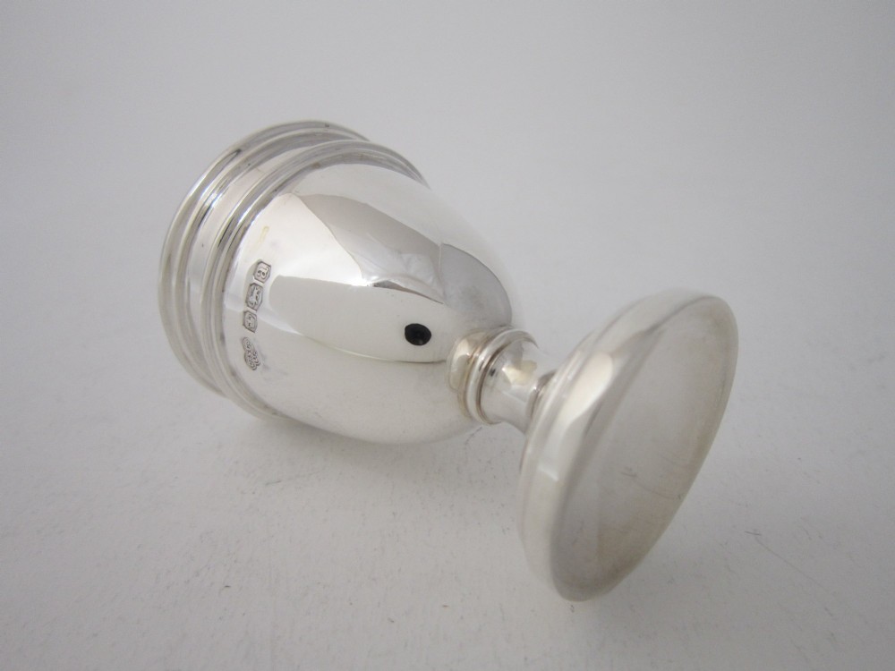 An antique George V sterling silver egg cruet featuring a central carrying handle, six egg cups, and matching spoons arranged on an oval tray base. View X