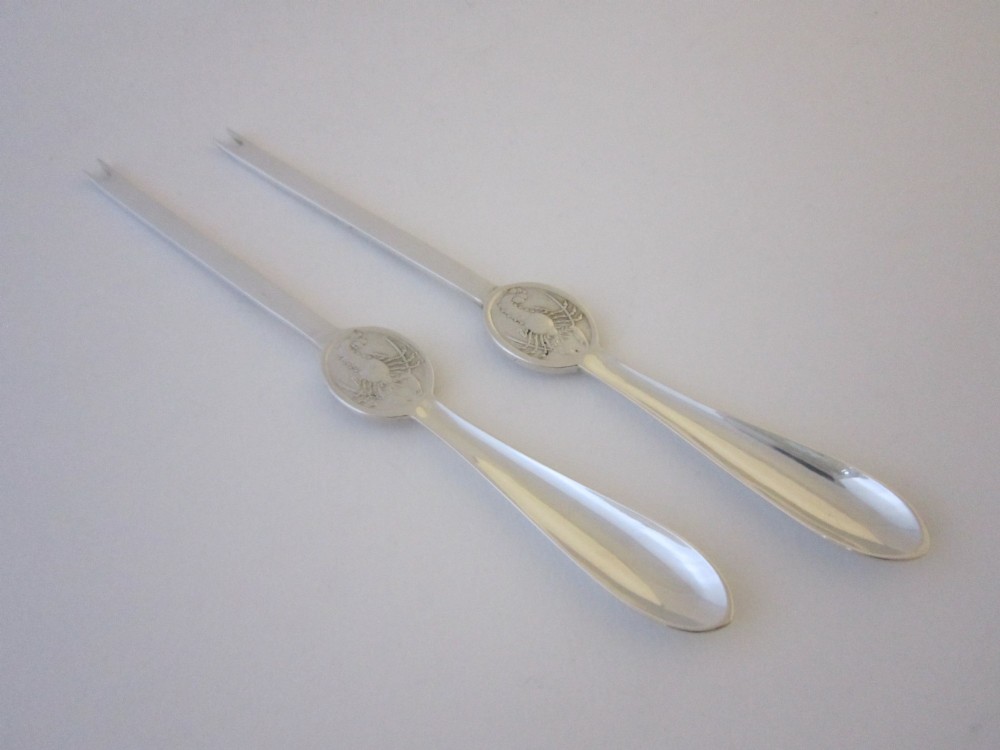 A pair of sterling silver lobster picks with embossed crustacean central medallions displayed inside a fitted black satin and velvet presentation box. View IV