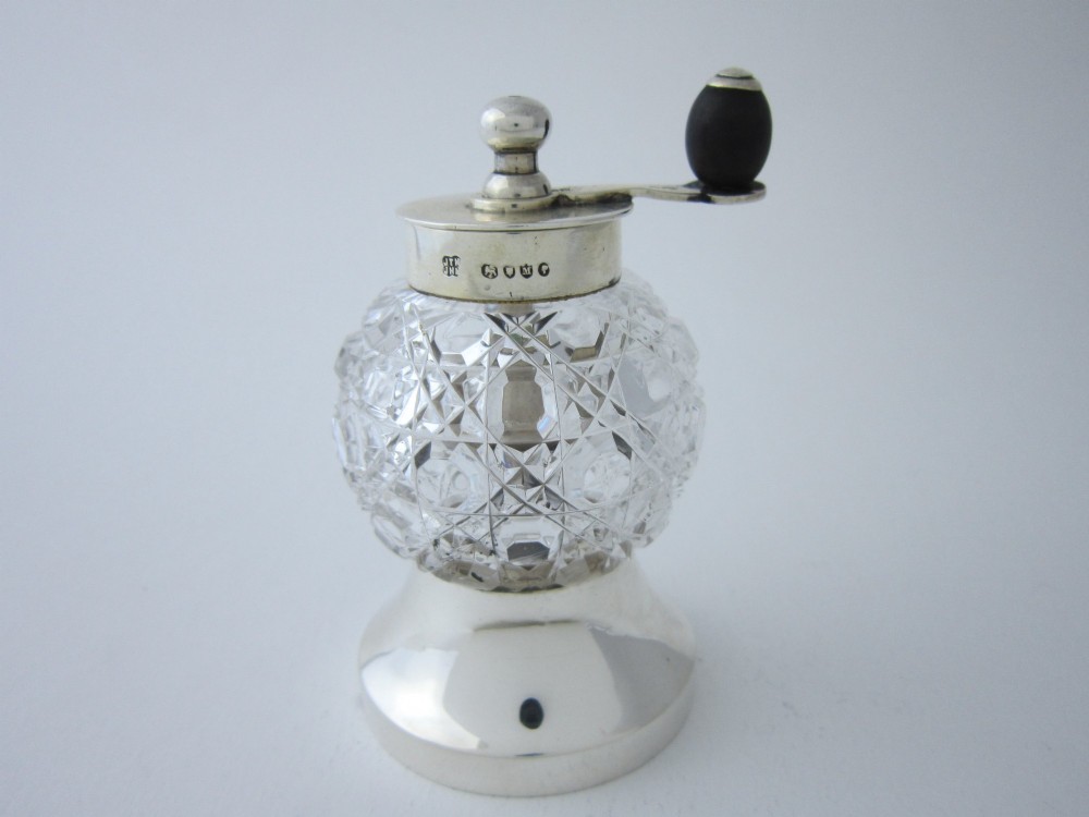 A Victorian sterling silver and cut glass pepper grinder featuring a round glass body, hallmarked silver collar and base, and a top crank handle.
