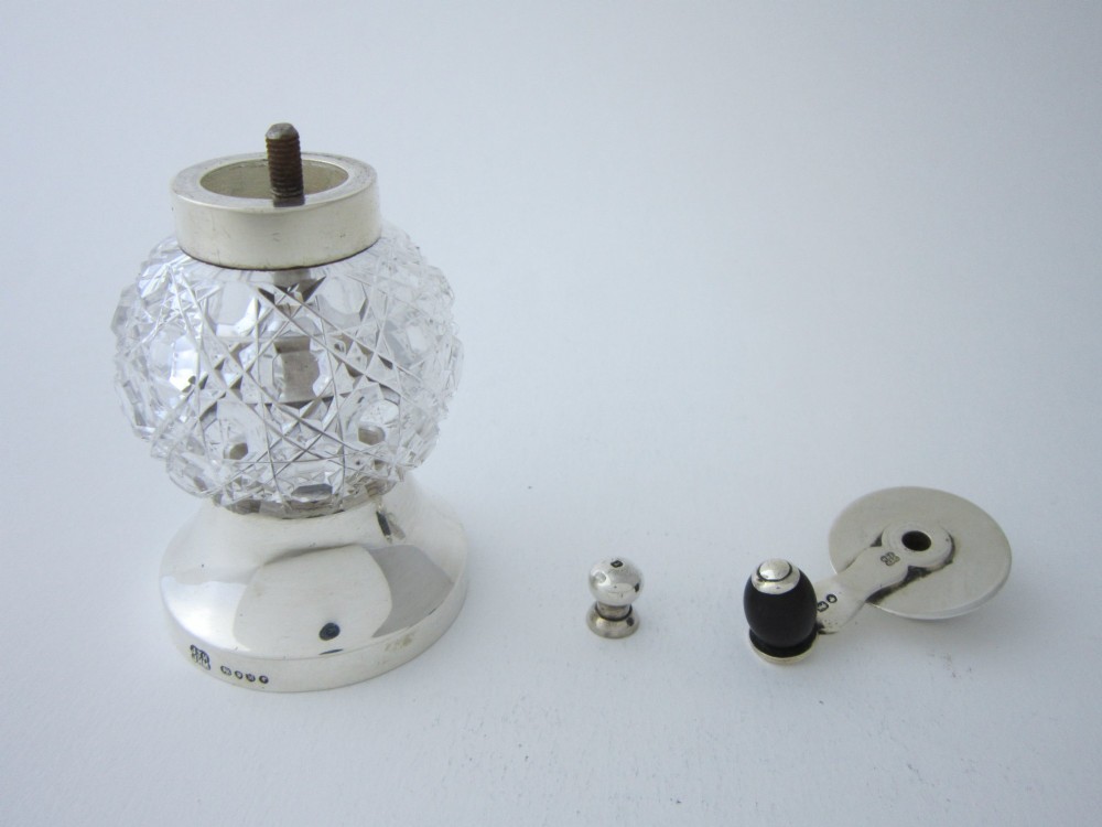 A Victorian sterling silver and cut glass pepper grinder featuring a round glass body, hallmarked silver collar and base, and a top crank handle. View V