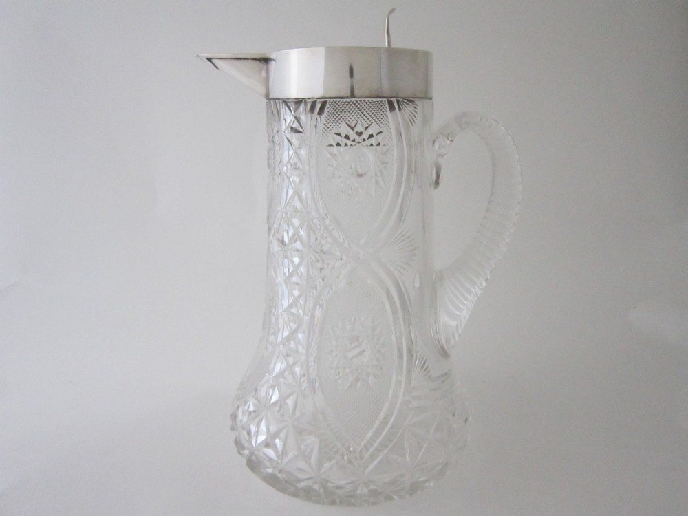 A large George V cut glass jug featuring a sterling silver collar and spout alongside a moulded glass handle.