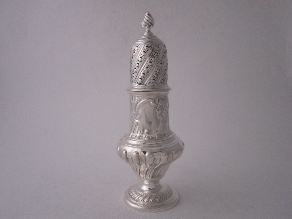 A Victorian sterling silver sugar caster featuring a spirally fluted pierced dome lid, a flame finial, and embossed cartouche detailing on a pedestal foot.