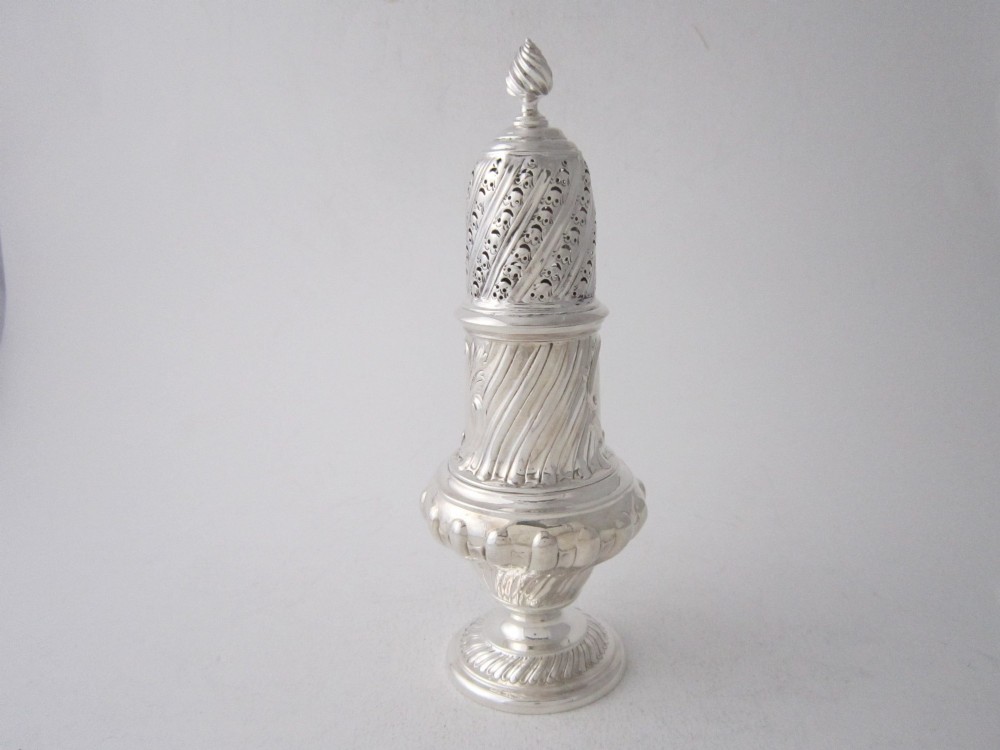 A Victorian sterling silver sugar caster featuring a spirally fluted pierced dome lid, a flame finial, and embossed cartouche detailing on a pedestal foot. View II