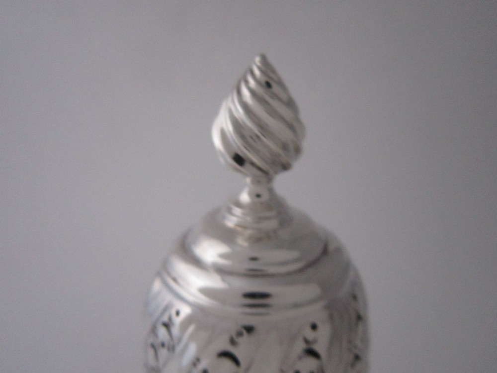 A Victorian sterling silver sugar caster featuring a spirally fluted pierced dome lid, a flame finial, and embossed cartouche detailing on a pedestal foot. View IV