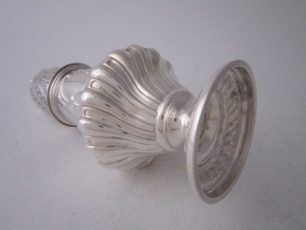 A Victorian sterling silver sugar caster featuring a spirally fluted pierced dome lid, a flame finial, and embossed cartouche detailing on a pedestal foot. View VII
