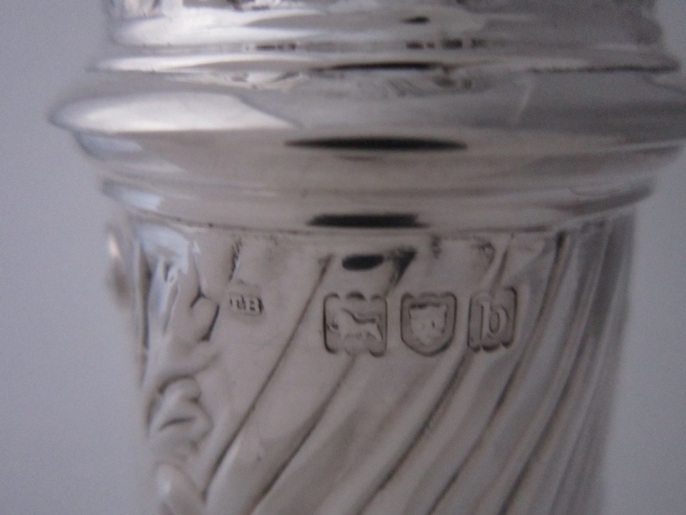 A Victorian sterling silver sugar caster featuring a spirally fluted pierced dome lid, a flame finial, and embossed cartouche detailing on a pedestal foot. View VIII