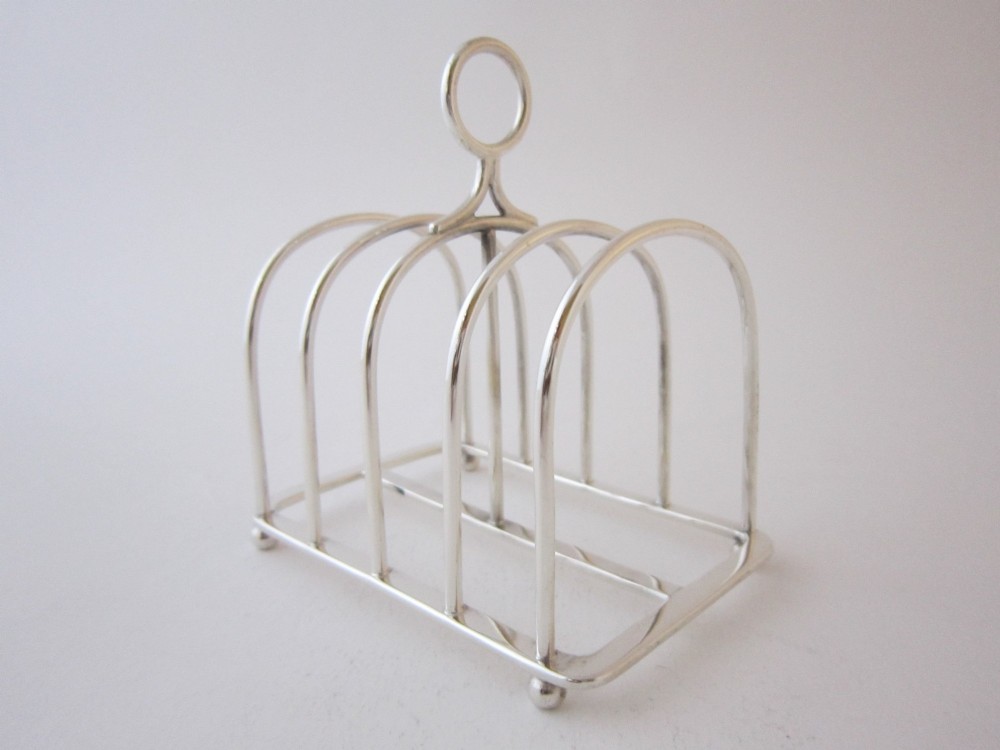 A Victorian sterling silver toast rack with five arched wire partitions, a top ring handle, and small ball feet.