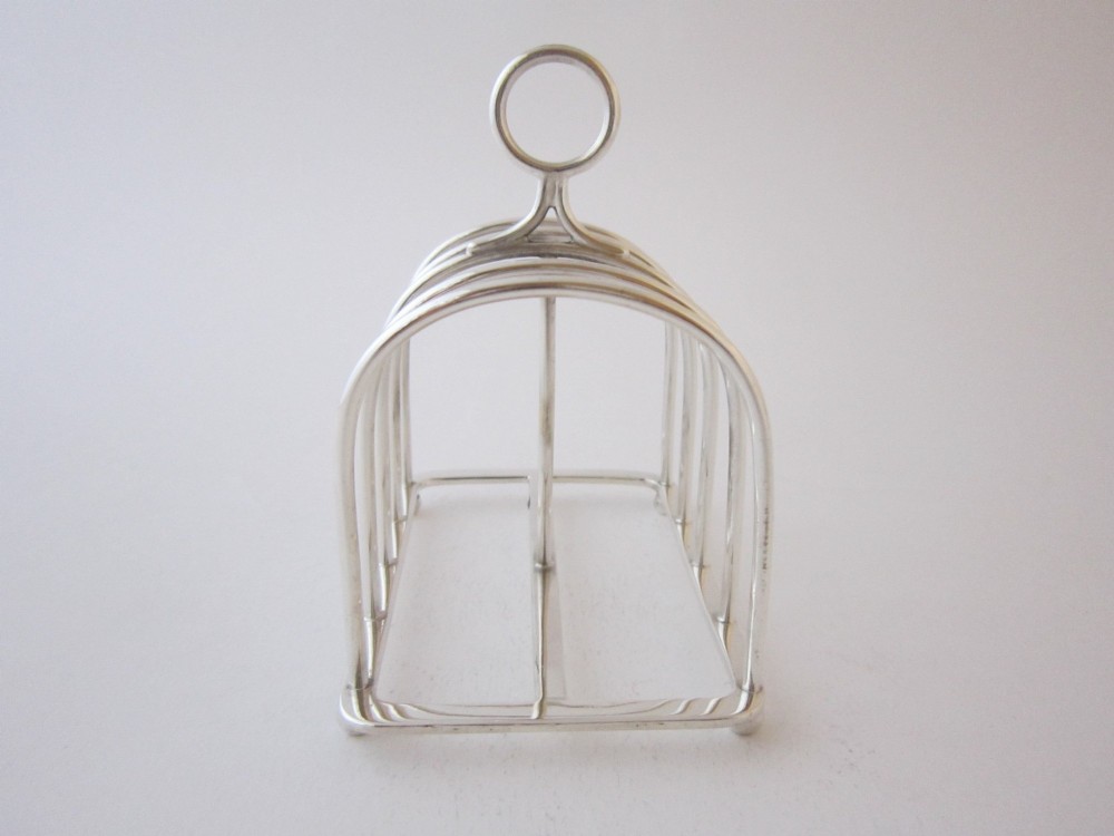 A Victorian sterling silver toast rack with five arched wire partitions, a top ring handle, and small ball feet. View II