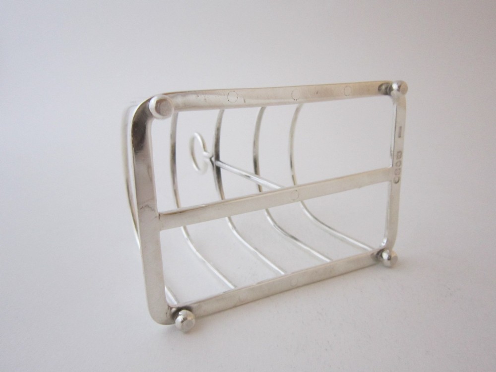 A Victorian sterling silver toast rack with five arched wire partitions, a top ring handle, and small ball feet. View V