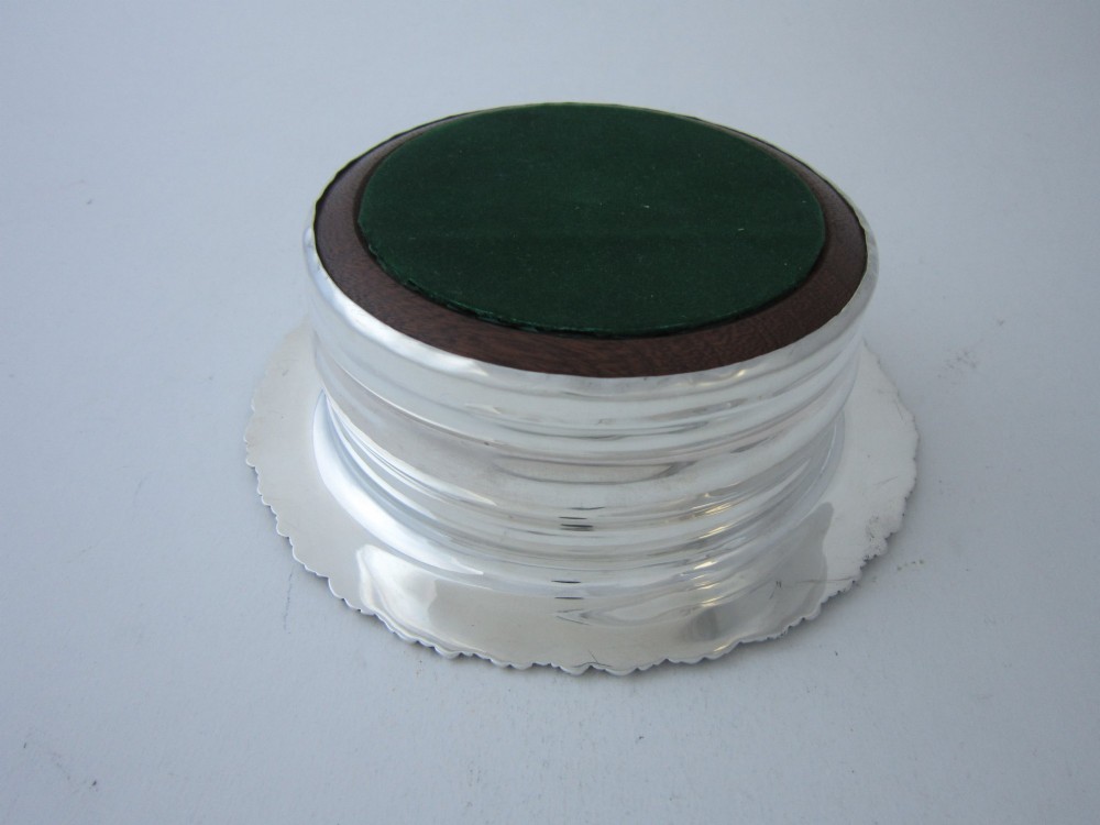 A circular George V sterling silver wine coaster featuring an ornate floral scroll rim and a polished stepped body with a wood insert base. View IV