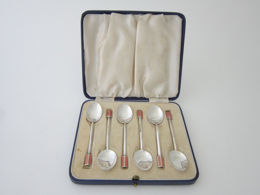 A set of six Art Deco sterling silver coffee spoons with pink enamelled terminals presented in an open blue silk and velvet lined case.