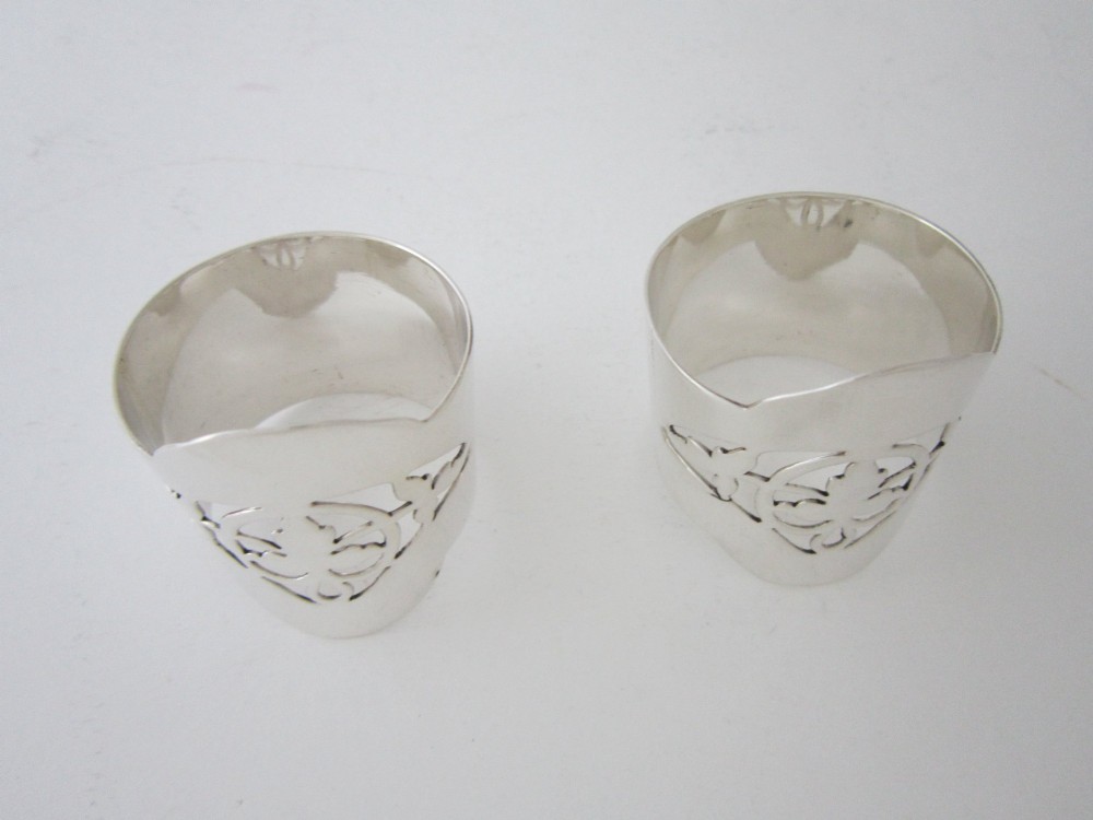 A pair of polished sterling silver napkin rings featuring pierced fretwork crest designs and shaped borders. View III